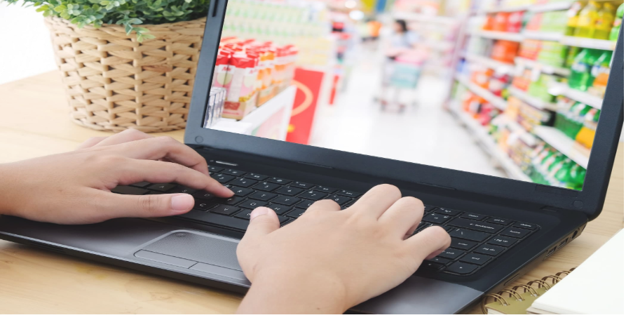person typing on their laptop with a grocery store on screen